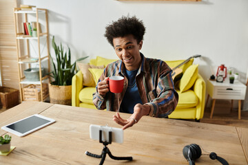 A young African American male blogger holding a cup of coffee while talking on a phone camera at a...