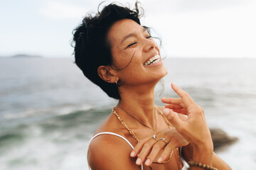 Carefree woman with wavy hair posing joyfully by the seaside beach