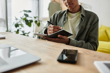 A young African American man focused on writing in a notebook at his desk.