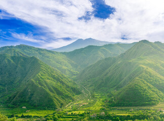 Fototapeta premium amazing view at a green landscape between two mountains with a high peak with snow and blue cloudy sky on background