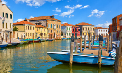 Murano Island in Venice, Italy. Boats by the piers and antique italian houses along channel. Blue...