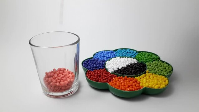 Pink peach masterbatch granules are poured into a shot glass, next to various other masterbatch colors in a palette. Color pigment carrier polymers in the plastics industry