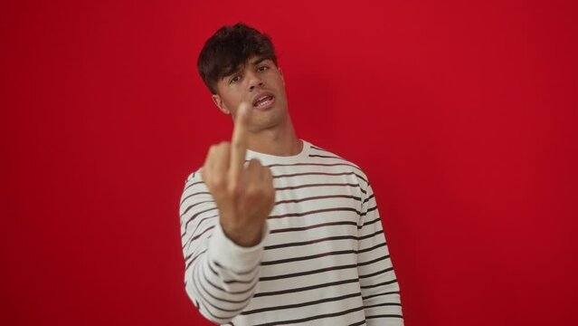 Fuck you middle finger young hispanic man wearing stripes t shirt standing, showing rude expression, impolite gesture over isolated red background