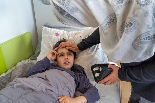 Anonymous mother checking hypoglycemic son's forehead in bedroom