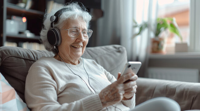 Elderly woman relaxing on the sofa, listening to music with headphones and holding an iPhone in her hand, enjoying leisure time at home