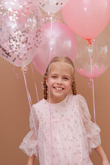 Smiling blonde girl in a dress with pink balloons. Vertical orientation.