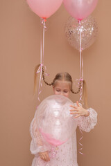 Girl with pigtails in a pink dress with balloons on a brown background. Vertical orientation.