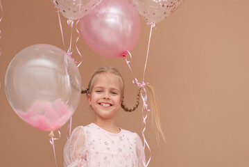 Smiling girl with pigtails in a dress with pink balloons on a brown background.