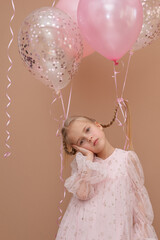 Pensive blonde girl with pigtails in a pink dress with balloons on a brown background. Vertical...