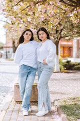 Fototapeta premium Two women are posing for a picture in front of a tree. They are wearing jeans and white shirts