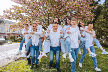 A group of young people are posing for a picture in front of a tree. Scene is lighthearted and fun, as the group is all wearing white shirts and jeans and are smiling for the camera