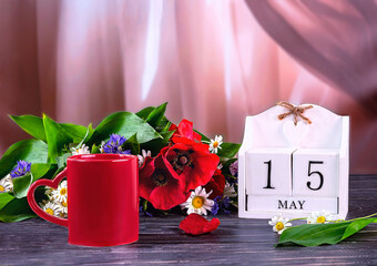 The calendar date is May 15. International Family Day. Composition with a bouquet of wild flowers, a wooden calendar, a red cup of coffee on the window.