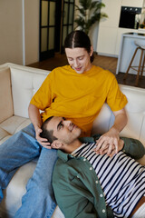Fototapeta premium A young gay couple shares a tender moment of intimacy on a couch in a modern apartment.
