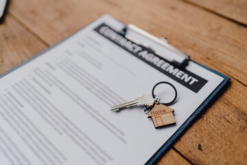 Close-up of a tenancy agreement document with a small house keychain on a wooden table, symbolizing...