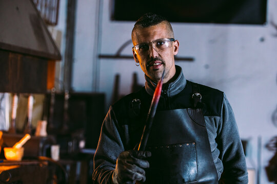 Confident blacksmith holding hot forged iron rod