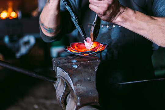 Blacksmith shaping a metal flower on anvil