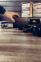 Retro cassette tape recorder with headphones and cassettes lying on wooden table and male hand pressing play button. Vintage cassette deck with tapes on wooden backdrop, perfect for nostalgic visuals