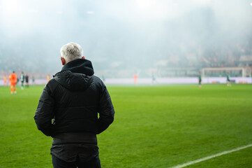 Head coach's back and soccer match at the stadium in the background.