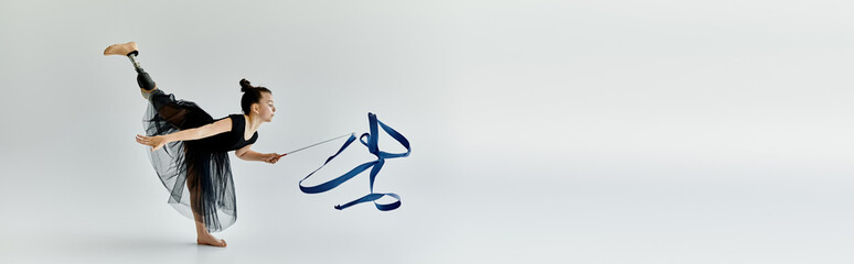 A young girl with a prosthetic leg performs a graceful ribbon routine in a gymnastics studio.