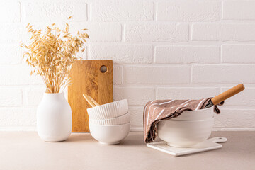 Set of white ceramic bowls for cooking on a stone kitchen countertop. a white vase with ears of wheat. A white brick wall. minimalism.