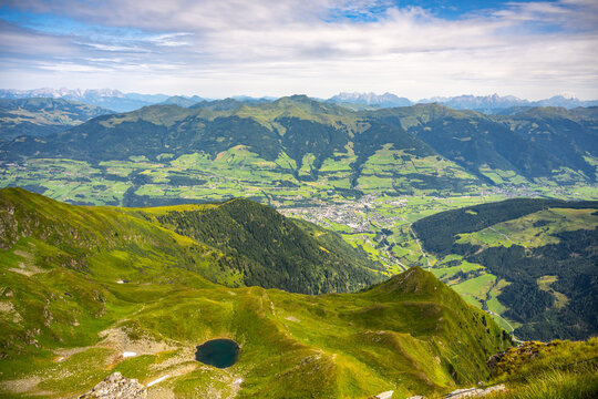 Overlooking the scenic Mittersill in Salzach Valley, Austrian alpine landscape with verdant hills and a small lake under a clear sky. Hohe Tauern National Park, Austria