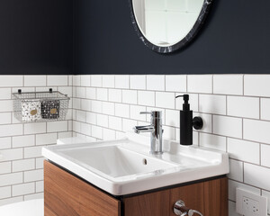 A bathroom sink detail with dark blue walls, subway tiles, a circular mirror, and a floating wood cabinet.