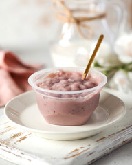 Currant whey dessert with spoon in plastic cup on board