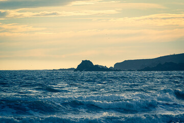 Waves rolling onto the beach, looking towards the rocks Howe Loup, with the sun low in the sky casting a golden light over Cruden Bay Beach, Aberdeenshire, Scotland on a cold New Year's Day.