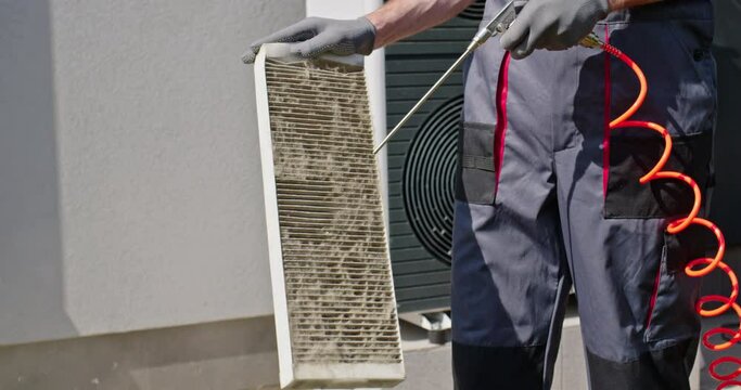 Worker cleaning a dirty air filter with a compressed air stream.