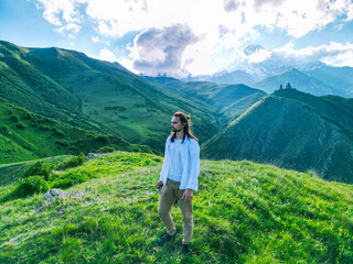 Naklejka premium long-haired man stands on the top of a green mountain in a white shirt - drone shot