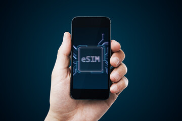 Close up of male hand holding cellphone with creative glowing eSim hologram on blurry background. Embedded sim and cellular mobile technology concept.