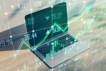 Close up of office workspace with laptop and growing green forex chart and arrows on blurry background. Index, finance and market growth concept. Double exposure.
