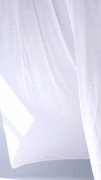 White transparent fabric flutters in the wind. Vertical. Long white curtains in a bright studio. Sheer white curtains blowing in the wind. slow motion. footage. A white curtain cascading in a sunlit r