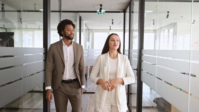 In a modern office corridor, an African-American businessman and his colleague are engaged in a lively discussion, walking together, reflecting a mentorship or collaborative work concept.