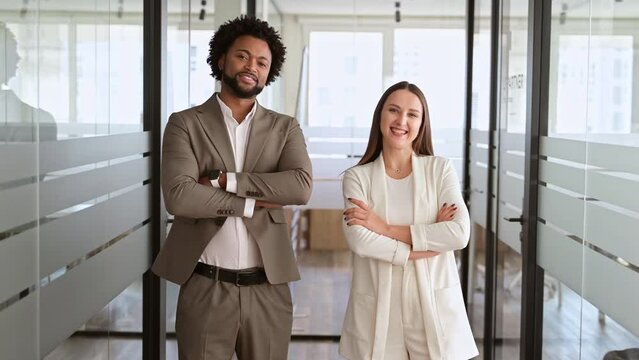 Standing confidently in a sleek office environment, a young businessman and businesswoman with their arms crossed exude professionalism and readiness. Spirit of equality and partnership