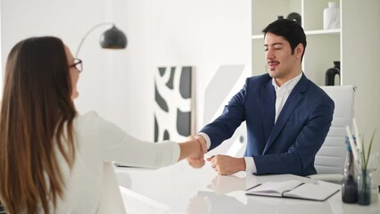 A man and a woman share a firm handshake in a contemporary office, suggesting the completion of a successful interview or business negotiation. A sense of professionalism and successful collaboration