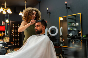 Expert barber meticulously trims and styles a man's hair using scissors, focusing on precision and...