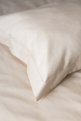 Beige pillow in satin or silk or lyocell pillowcase on beige sheet. Bedding and accessories. Home textile