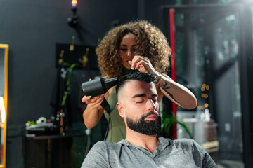 A man enjoys a relaxing moment in a barber's chair, reading the newspaper while getting a professional hair drying and styling at a modern barbershop.