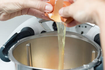 Hands cracking an egg into a mixer bowl for baking, white stand mixer, metallic bowl, focused on action