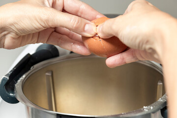 a pair of hands cracking an egg into a pot of boiling water, likely for poaching