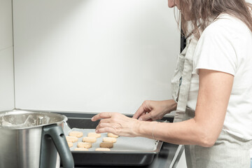 a person arranging unbaked cookies on a tray beside a mixing bowl in a white kitchen