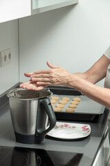 hands dusting flour over a kitchen blender with cookie dough, indicating baking preparation on a modern stovetop