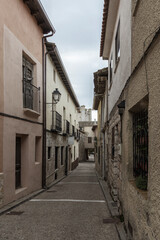 A narrow, stone-paved street flanked by old, textured buildings under a cloudy sky in a historic town