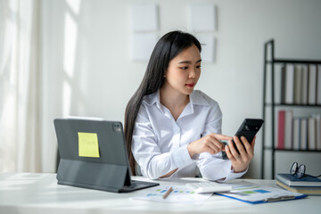 A woman is sitting at a desk with a computer and a cell phone