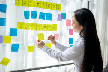 A woman is writing on a board with yellow and pink post it notes