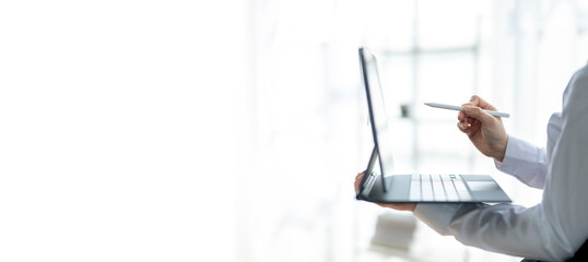 A person is holding a pen and writing on a laptop