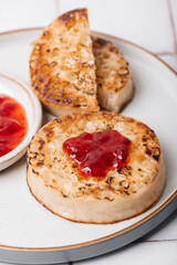 Hot Toasted Crumpets with piece of butter on a plate with strawberry jam. Perfect tasty breakfast popular in England, UK