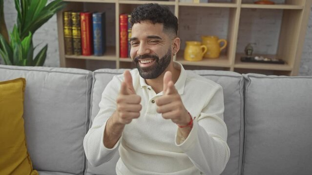 Energetic young hispanic man at home, pointing finger towards camera with a happy, funny expression, radiating good vibes