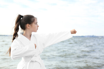 Cute little girl in kimono practicing karate near river